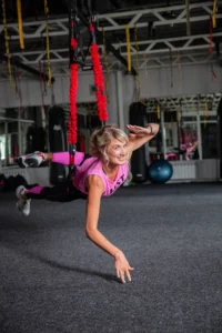 woman in pink shirt hanging from ceiling bungee cords working out